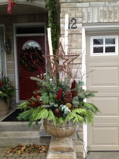 a planter filled with pine cones and greenery on the front steps of a house