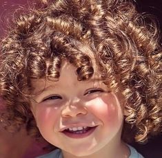 Gros plan du visage souriant d'un jeune enfant aux cheveux bouclés dorés, avec des joues rosées et un large sourire sincère qui illumine son visage