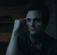 a man sitting in front of a bookshelf with his hand on his head