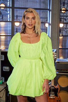 a woman in a neon green dress posing for the camera with an electric guitar behind her