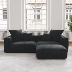 a black couch sitting in front of a window next to a plant on the floor