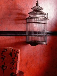 a birdcage hanging from the side of a red wall