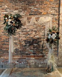 two tall vases filled with flowers on top of a rug next to a brick wall