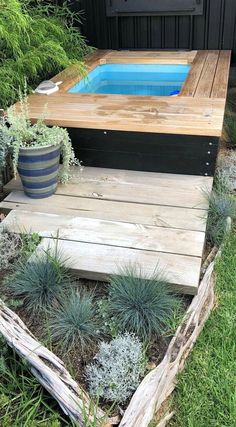 an outdoor hot tub in the middle of some grass and plants next to a wooden deck