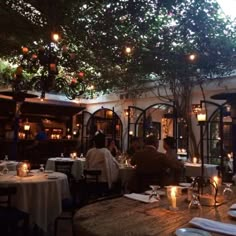 people sitting at tables in an outdoor restaurant with lit candles on the tables and trees overhead