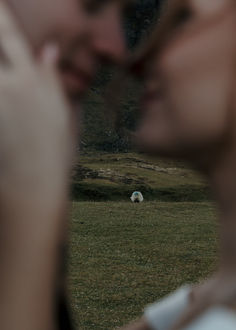 a woman with her hand on her face looking at a sheep in the field behind her