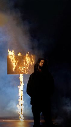 a man standing in front of a cross on fire