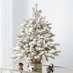 a small white christmas tree sitting on top of a glass table next to two cats