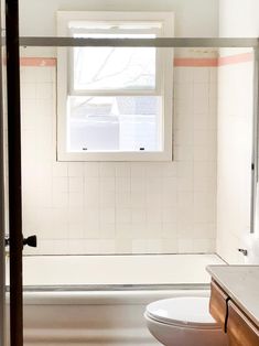 a white toilet sitting under a window next to a sink and bathtub in a bathroom