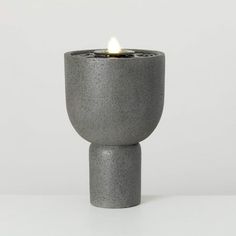 a grey candle holder with a lit candle in it