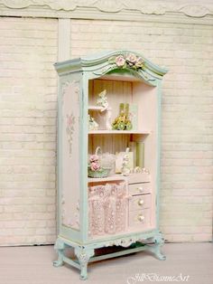 an old fashioned china cabinet painted in pastel blue and pink with flowers on the top shelf