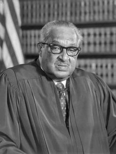 an older man wearing glasses sitting in front of a flag