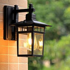 an outdoor light on the side of a brick wall with trees in the back ground