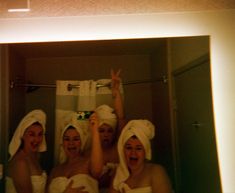 three women in towels standing in front of a mirror with their hands up to the ceiling