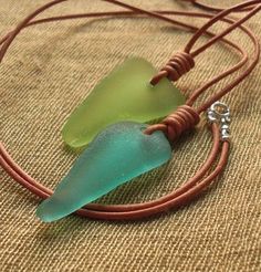 two pieces of glass sitting on top of a brown cord with a silver charm hanging from it