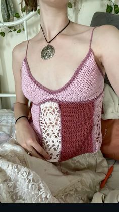 a woman sitting on a bed wearing a crocheted tank top and holding an object in her hand