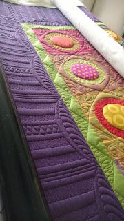 a quilted bed spread on top of a white bed with purple and yellow designs