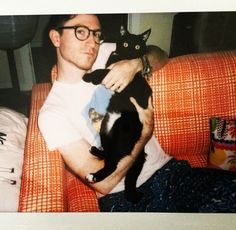 a man is holding a black cat on his lap while sitting in an orange chair