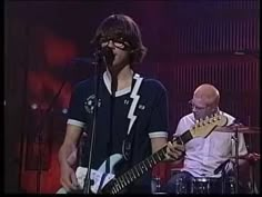 two men on stage with guitars and one man in the foreground playing an instrument