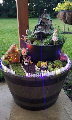 a fairy garden in a barrel on the side of a house with lights coming from it