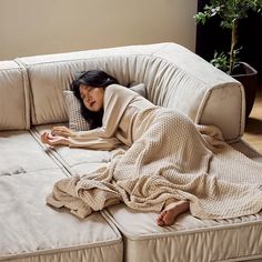 a woman laying on top of a couch covered in a blanket