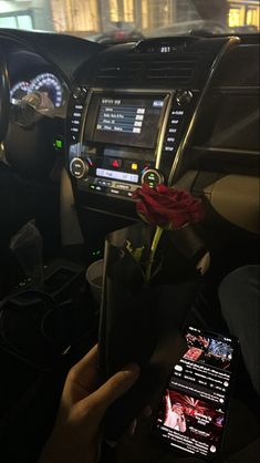 someone is holding a rose in their hand while sitting in the driver's seat