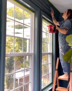 a woman standing on a ladder painting the windows with blue paint and holding a red cup in her hand