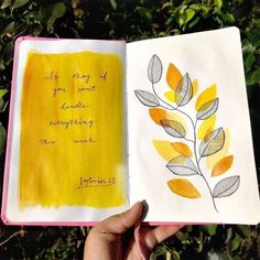 a hand holding an open book with watercolors and writing on the inside pages