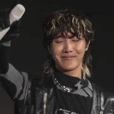 a woman with curly hair wearing a black shirt and leather jacket holding a white object in her right hand