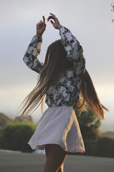 a woman with long hair is standing on a skateboard and holding her hands up in the air