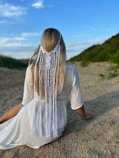 a woman sitting in the sand with her back to the camera and wearing a white dress