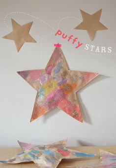 three paper stars are hanging on the wall next to some crafting materials and a sign that says puffy stars