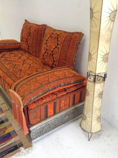 a bed with orange sheets and pillows next to a tall decorative object on the floor