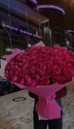 a woman holding a large bouquet of red roses in front of her face and wearing a pink shirt