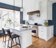 a white kitchen with blue walls and wooden flooring is pictured in this image, there are three stools at the center of the island