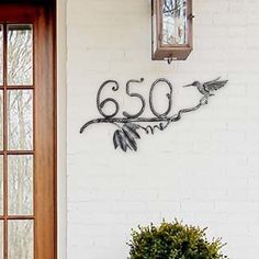 a house number sign on the wall next to a potted plant with flowers in it