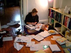 a woman is sitting on the floor with papers all over her and reading a book