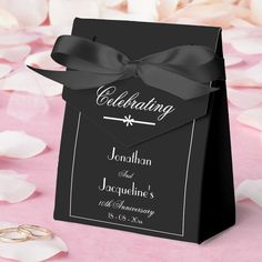 a black and white wedding gift bag with a ribbon on it, surrounded by petals