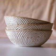 three white bowls sitting side by side on a counter top with a pink cloth behind them