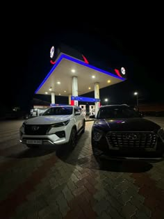 two cars are parked in front of a gas station at night with the lights on