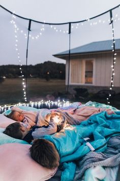 two people laying in bed with lights strung above them