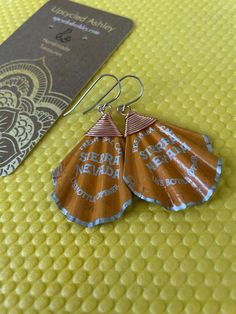 an orange and blue pair of earrings sitting on top of a yellow surface next to a passport