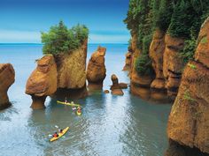 two people in kayaks paddling through the water near large rock formations and trees