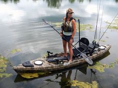 a woman standing on top of a kayak holding a fishing pole and two rods