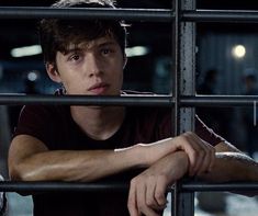 a young man leaning on the bars of a jail cell, staring at the camera