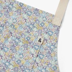 the back side of an apron with a flower pattern on it and a white tag hanging from