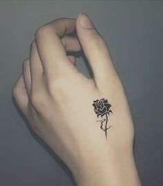 a woman's left hand with a small black rose tattoo on it