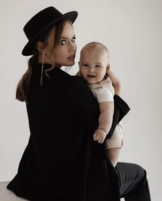 a woman holding a baby in her arms and wearing a black hat on top of her head