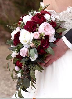 a close up of a person holding a wedding bouquet with red and white flowers on it