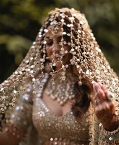 a woman in a gold and silver dress with beads on her head, holding out her hands